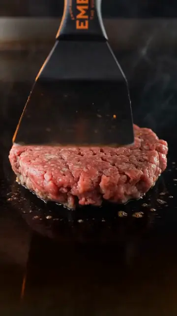 A spatula presses a burger patty onto a hot griddle.