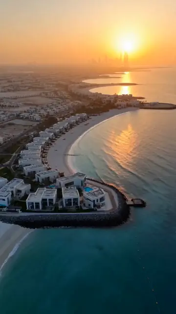 Beachfront villas on a curved shoreline at sunset.